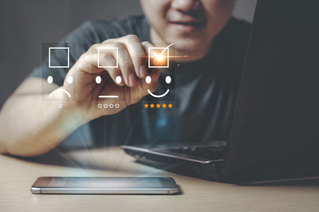 Young Asian Businessman give a happy smile and five star shape on a virtual digital screen with smartphone and laptop, the concept of surveying rating satisfaction.